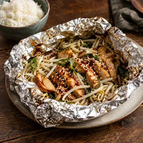 Kipfilet met taugé, ketjap en sesamzaad uit een geopend foliepakketje.